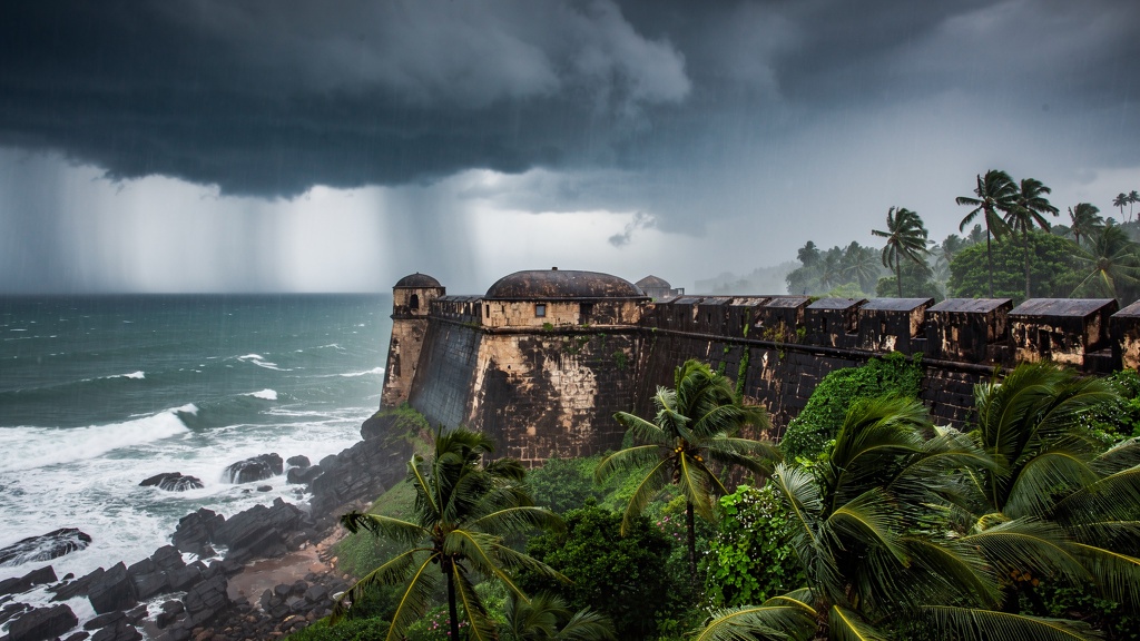 Dramatic monsoon clouds gather over a coastal fort with lush palms